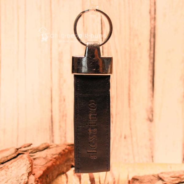 Detailaufnahme der destino Prägung auf dem 3 cm breiten Taschenanhänger aus Echtleder.